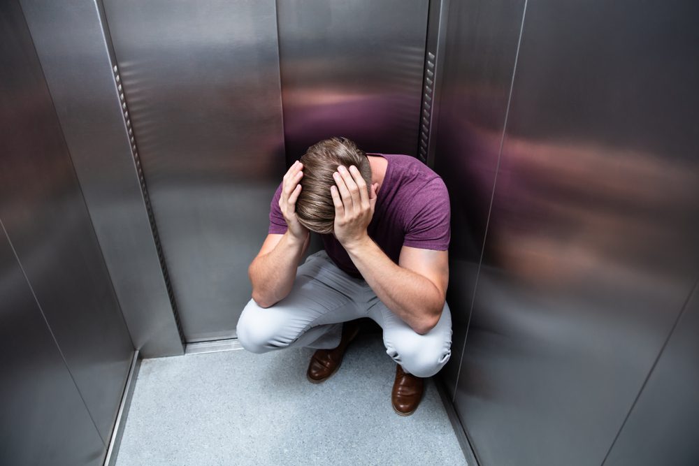 Crouched,Worried,Man,With,Hands,On,Head,In,Elevator